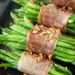 Prosciutto-wrapped green bean bundles on a dark platter