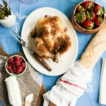 Whole rotisserie-style chicken on a white platter with strawberries and raspberries