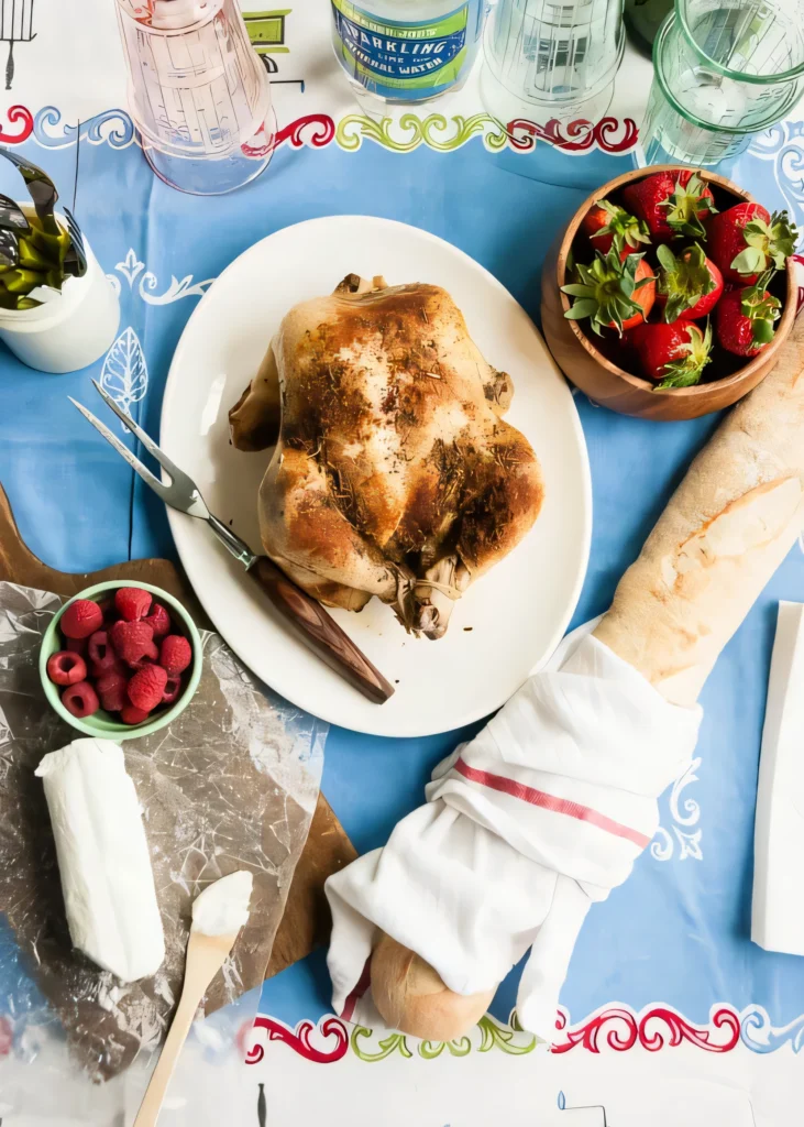 Whole rotisserie-style chicken on a white platter with strawberries and raspberries