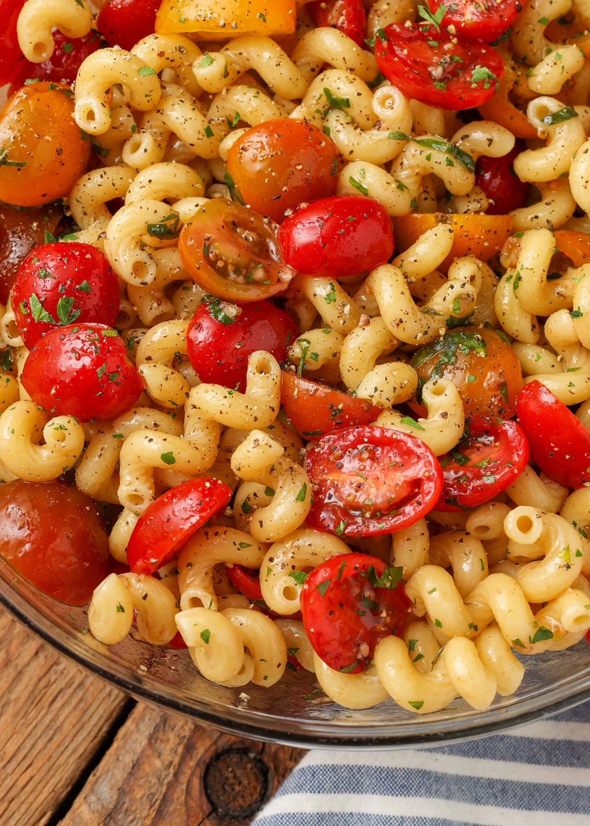 Hand tossing warm pasta with marinated tomatoes in a bowl