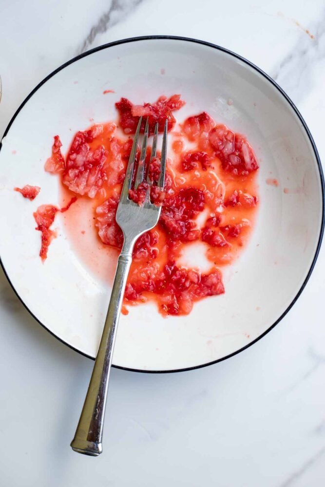 Fork mashing fresh strawberries on a plate