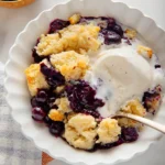 Warm blueberry cobbler with almond topping and vanilla ice cream in a bowl