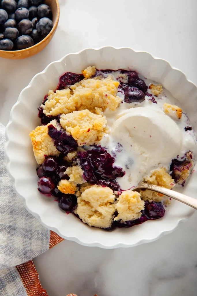Warm blueberry cobbler with almond topping and vanilla ice cream in a bowl