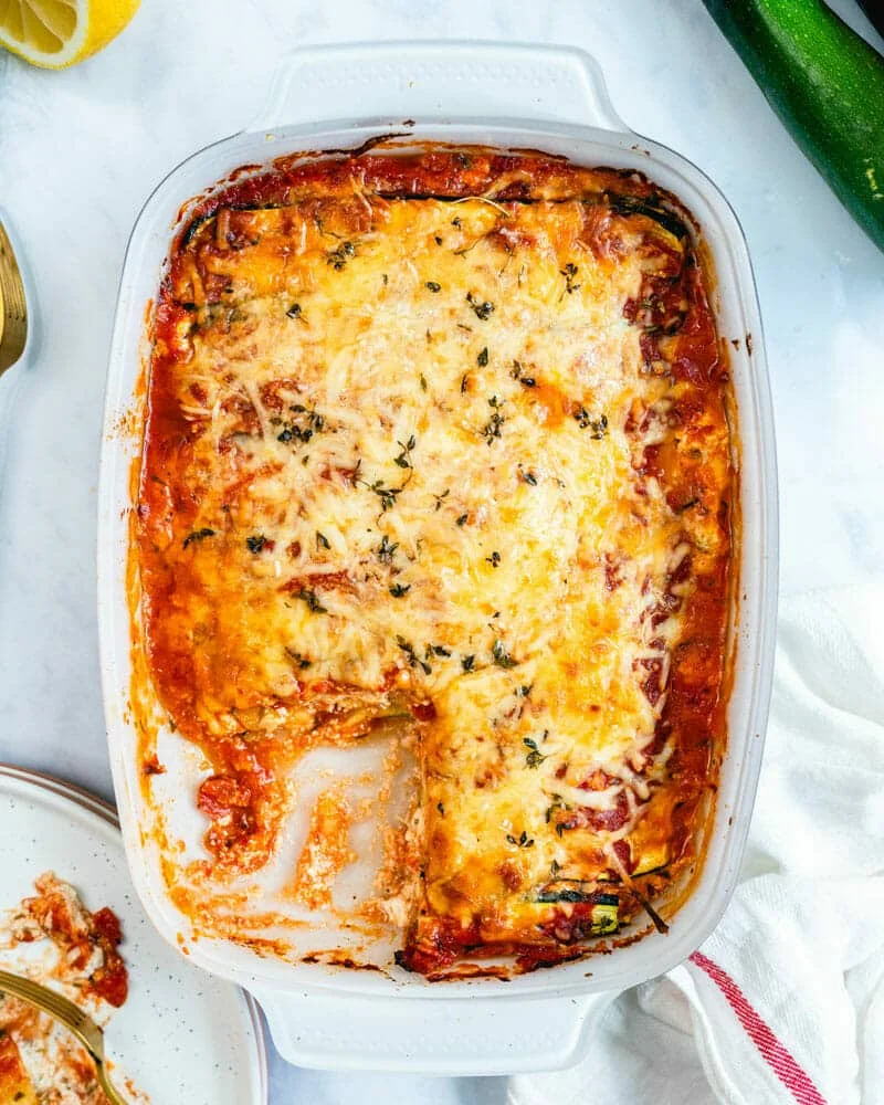 Baked zucchini lasagna with melted cheese and herbs in a white dish