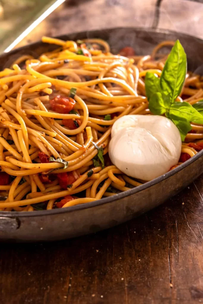 Burst cherry tomato pasta with burrata and basil in a dark skillet
