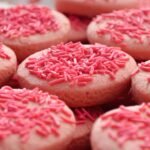 Pink-frosted cookies topped with pink sprinkle jimmies, close-up