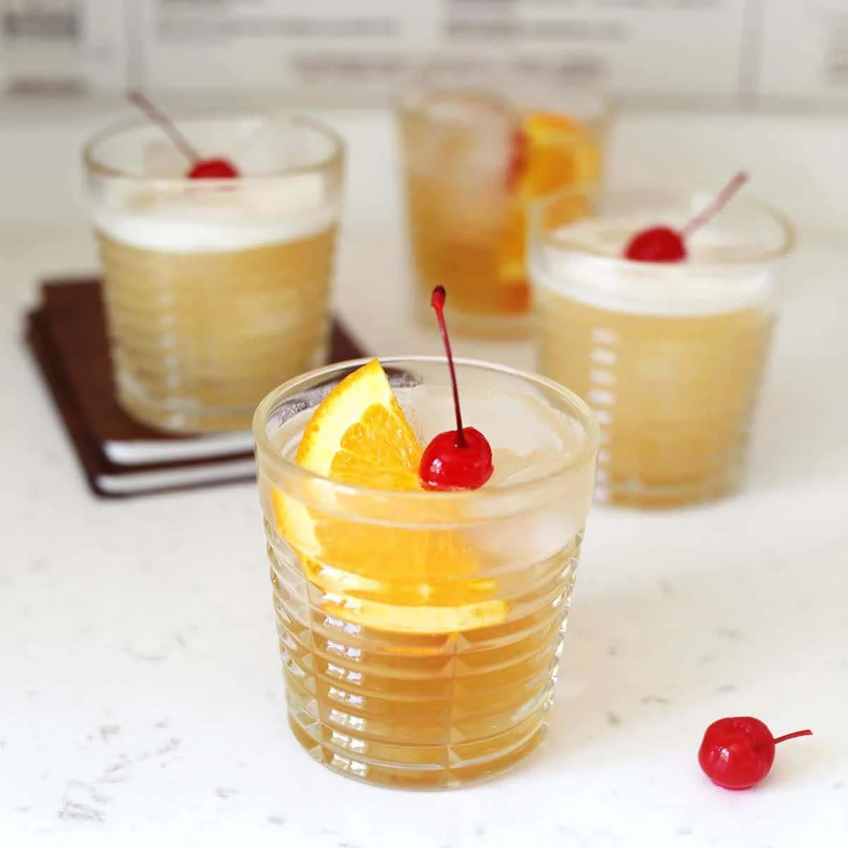 Two amaretto sours garnished with cherries and orange wedges