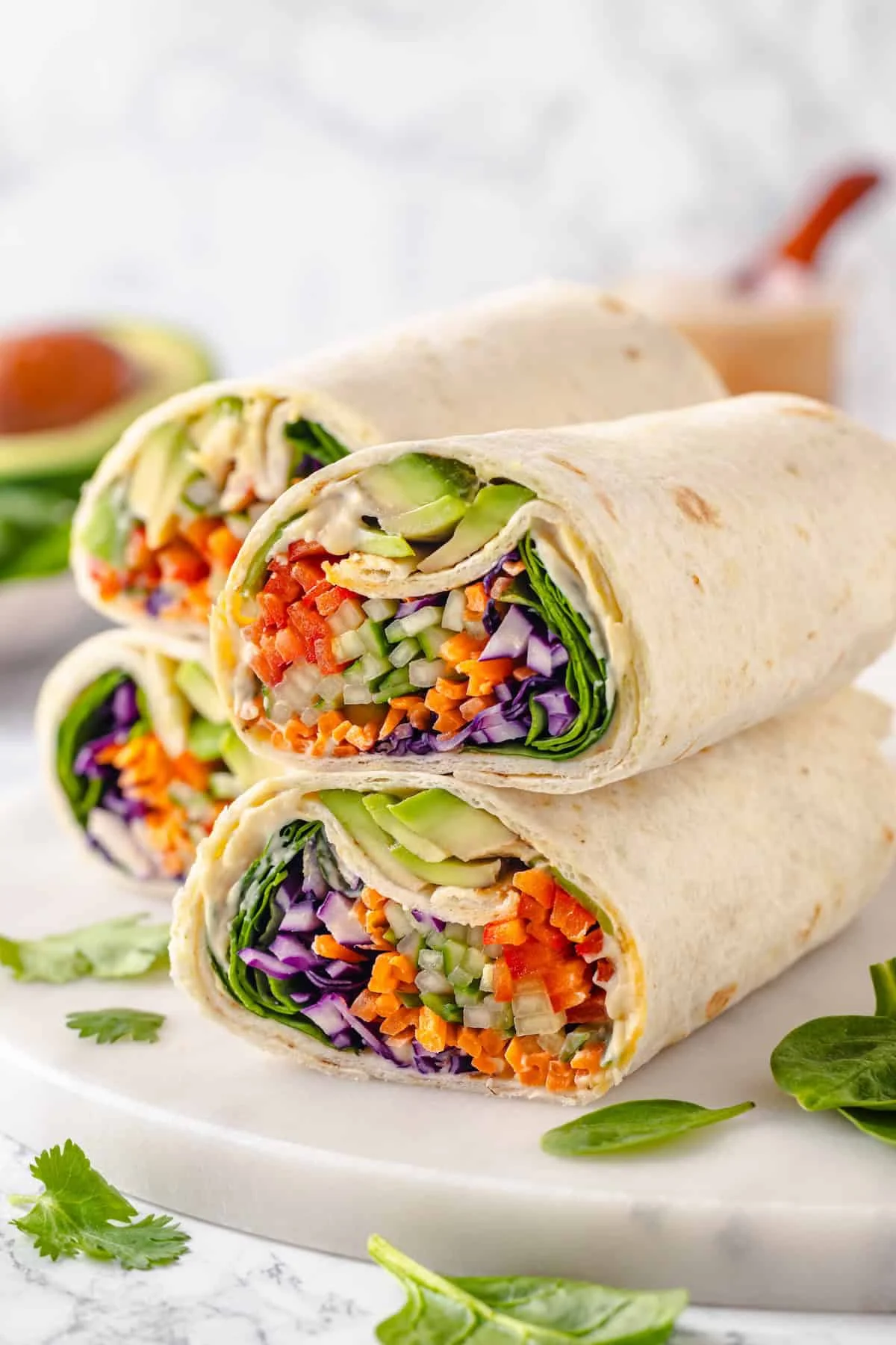 Colourful no-cook veggie wraps cut in half, showing hummus, avocado and rainbow vegetables.
