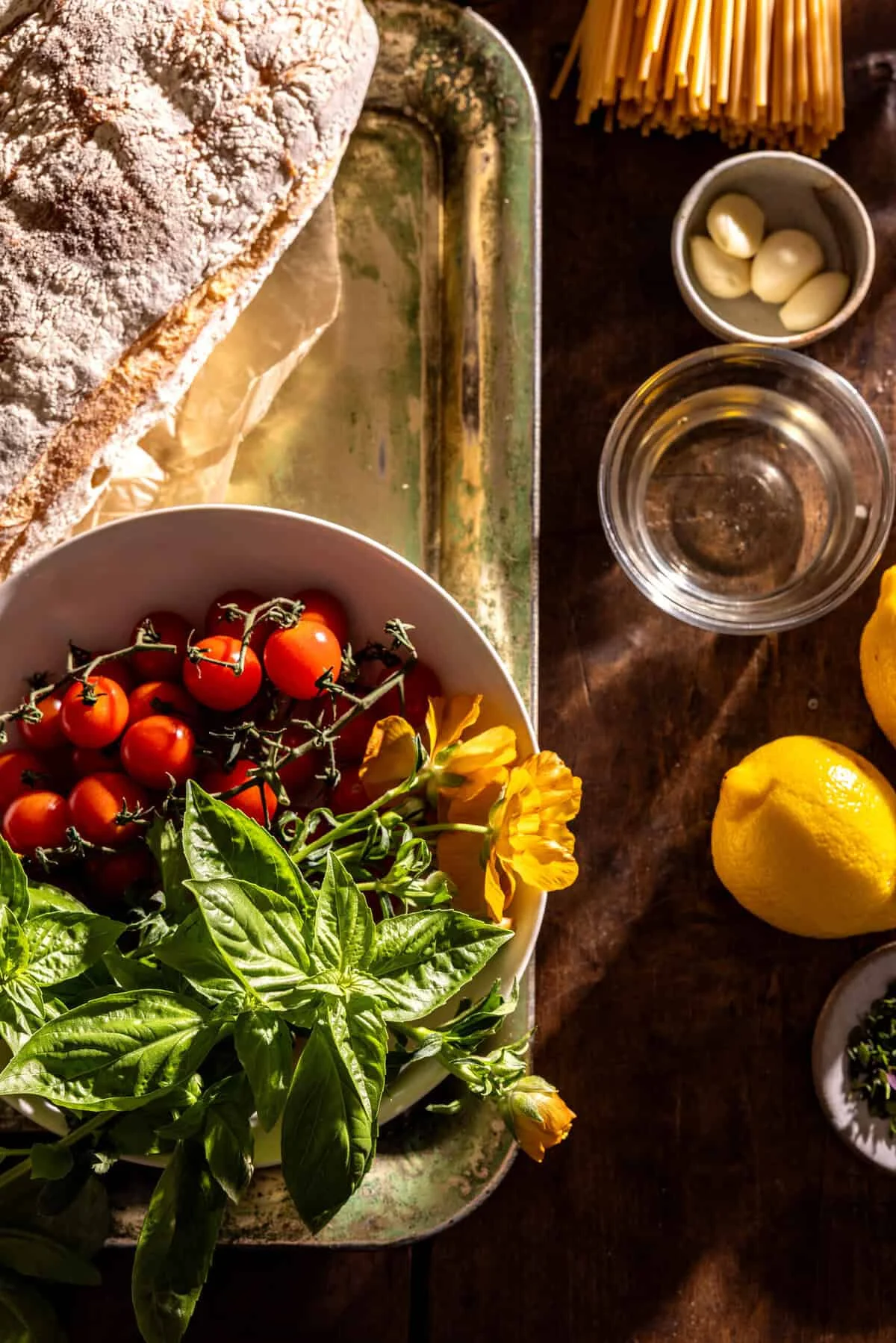 Cherry tomatoes, ciabatta, basil, lemon and garlic arranged on dark wood