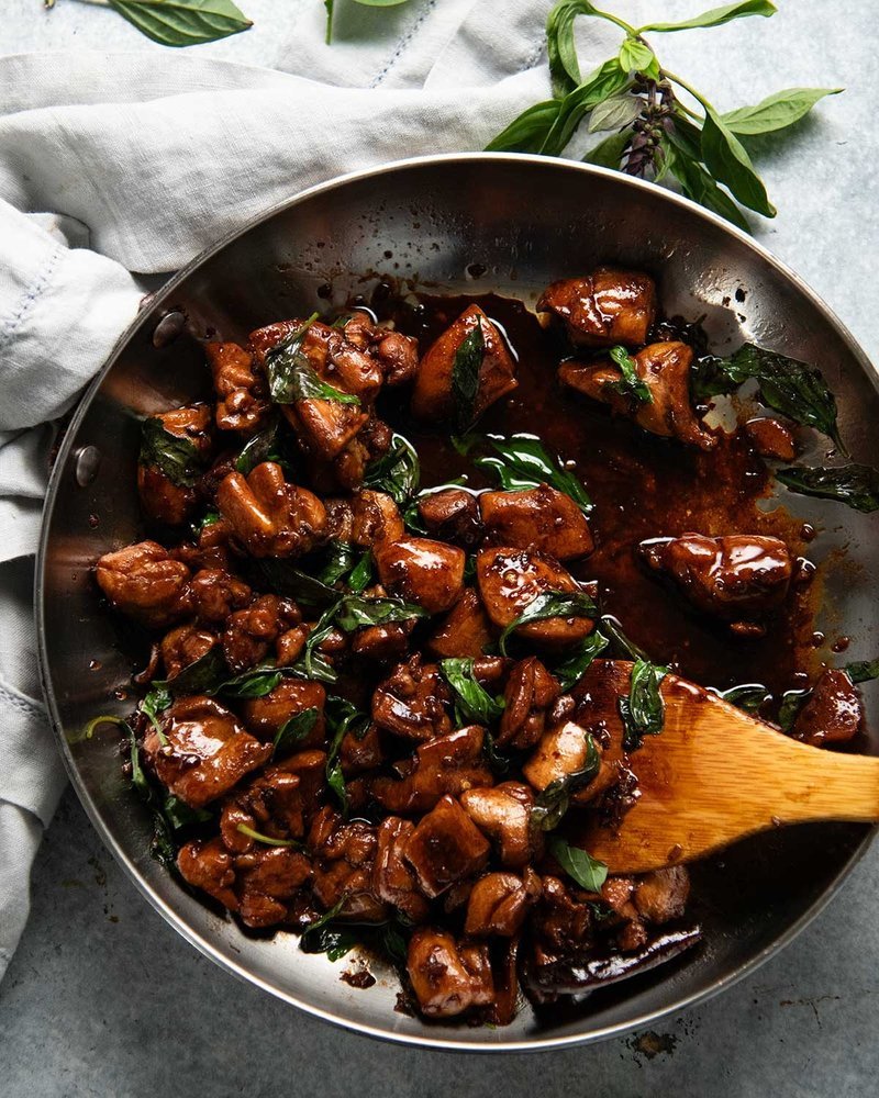 Chicken braised in glossy soy sauce in a pan with Thai basil