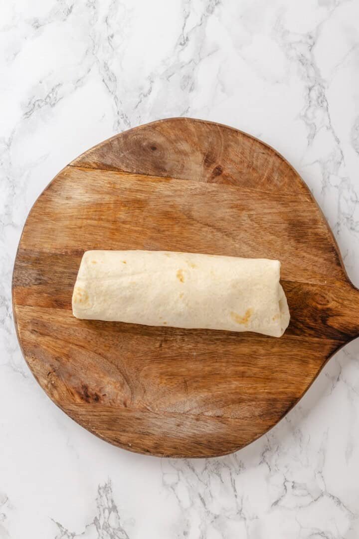 Rolling a filled tortilla into a tightly wound veggie wrap.