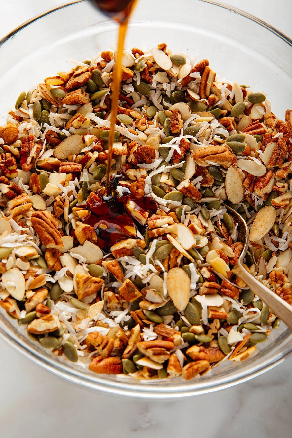 Maple syrup being poured over the dry granola mixture